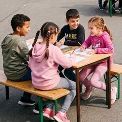 Kinder sitzen gemeinsam am Tisch und erledigen Hausaufgaben im Hort, konzentriertes Lernen, Zusammenarbeit und pädagogische Unterstützung in der Nachmittagsbetreuung.