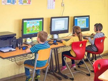 Grundschüler sitzen am Computer im Klassenraum und lösen Aufgaben am Bildschirm
